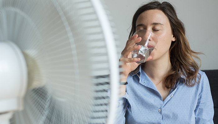 Woman shown sitting in front of fan during summer heat in Erie, PA.