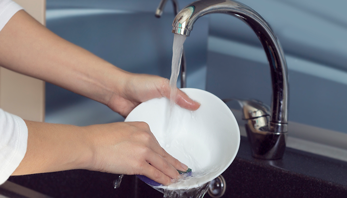 Hot water from a tankless water heater is used to wash dishes in a kitchen sink.